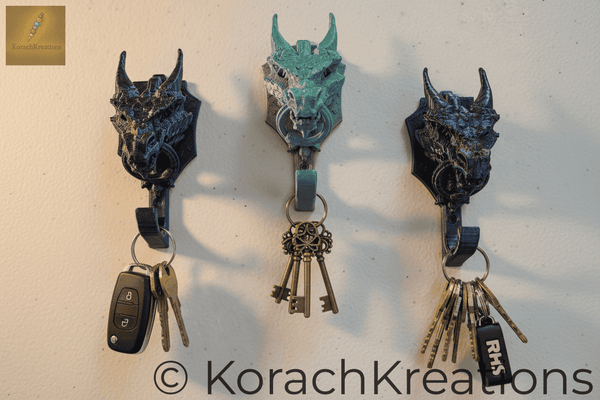 Multiple 3D printed dragon key holders mounted on a wall spaced apart, each holding a different set of keys, warm natural lighting